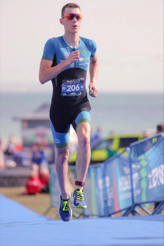 Jamie running in a triathlon, race number 206, seafront behind.