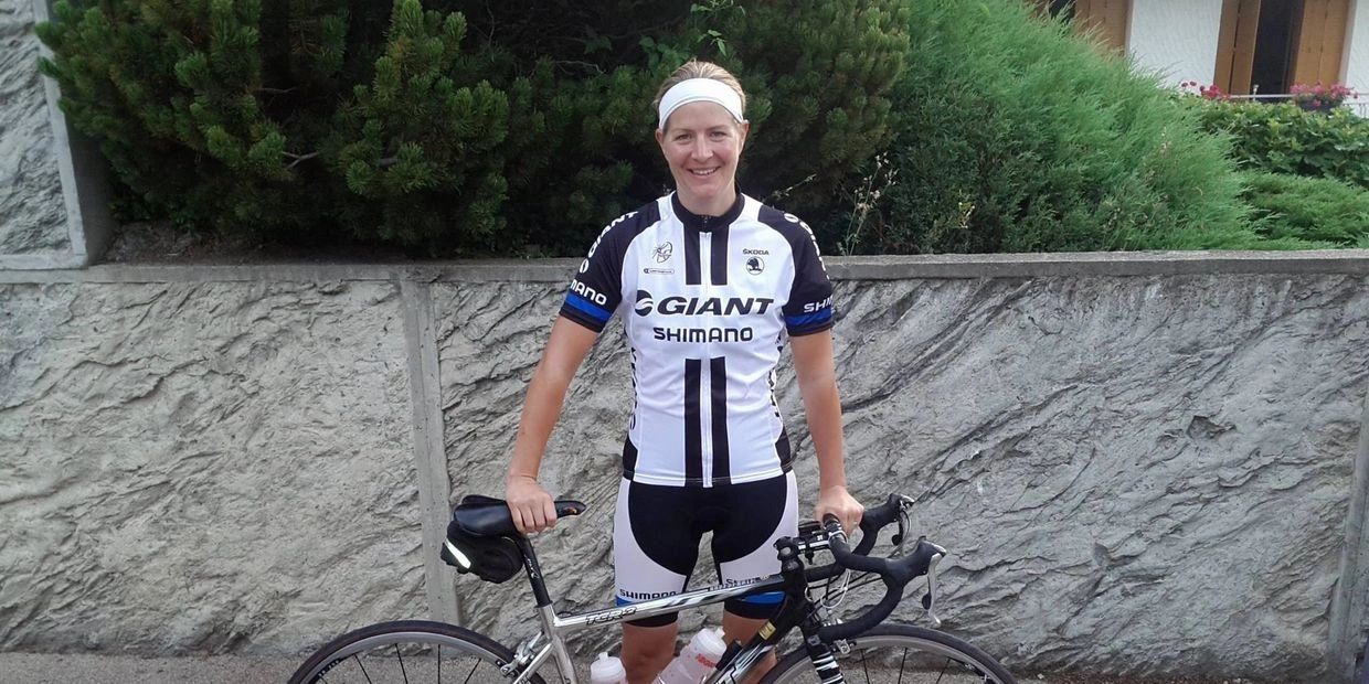 Karen Jaques in Giant/Shimano team cycling kit, standing with her road bike against a stone wall.